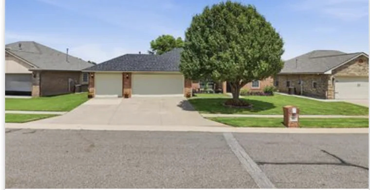Single-story brick home with a two-car garage and a mature front-yard tree in Edmond