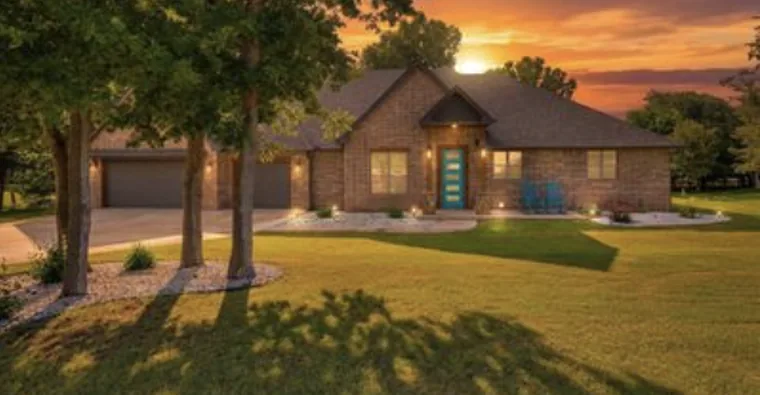 Brick home with a three-car garage on a treed lot at sunset in Guthrie